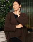 Woman wearing a brown wrap knitwear standing next to a plant indoors