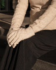 Person wearing a beige sweater, dark pants, and gloves sitting on steps.