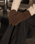 Person wearing brown gloves and dark pinstripe pants sitting on a black chair.