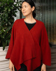 Woman wearing a red knitted poncho standing next to a plant
