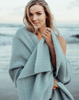 A woman smiling and wrapping a light blue alpaca wool shawl around her shoulders.