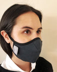 Woman wearing a black travel mask with adjustable elastic straps, made from merino soft & comfort next to skin, with a label showing 'Made in New Zealand', and highlighting features such as 100% breathable, adjustable elastic straps, and a machine washable filter.