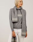 Woman wearing a gray sweater and patterned scarf against a plain background