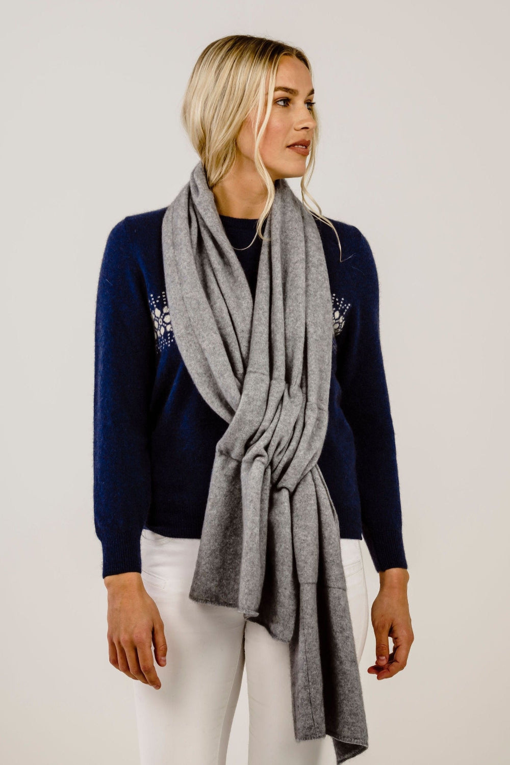 Woman wearing a navy sweater with a floral design and a gray scarf on a plain background