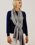 Woman wearing a navy sweater with a floral design and a gray scarf on a plain background
