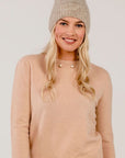 Woman wearing a pink sweater and knit beanie on a plain background