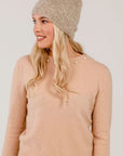 Woman wearing a beige knit beanie and sweater against a plain background