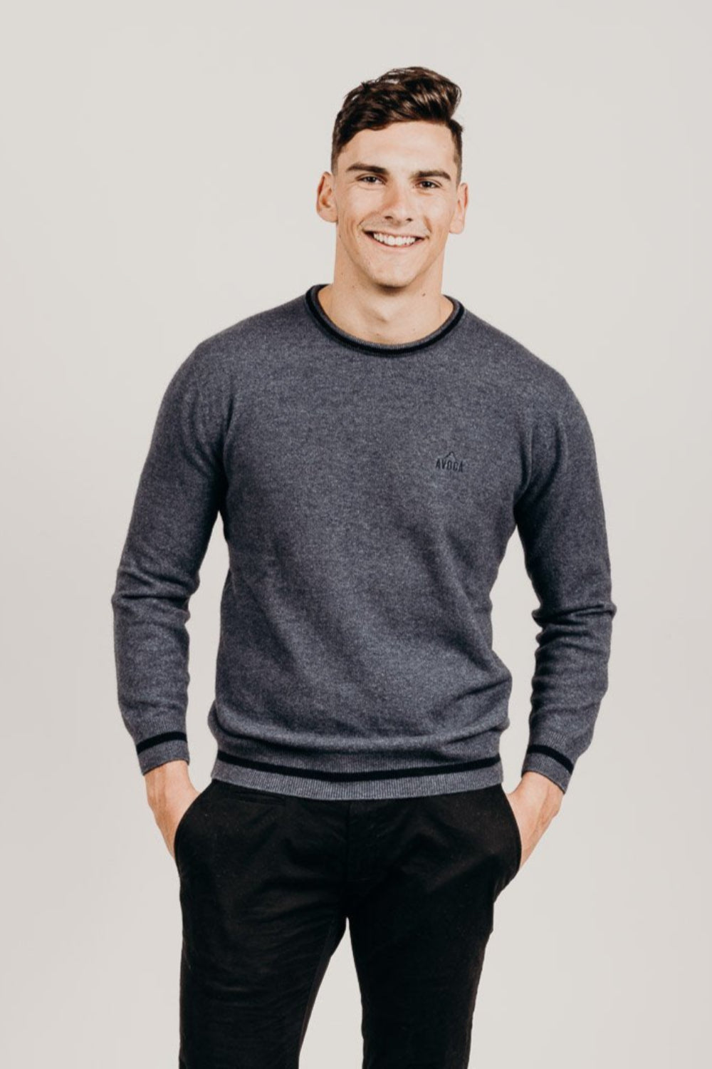 Man wearing a gray sweater and black pants against a plain background