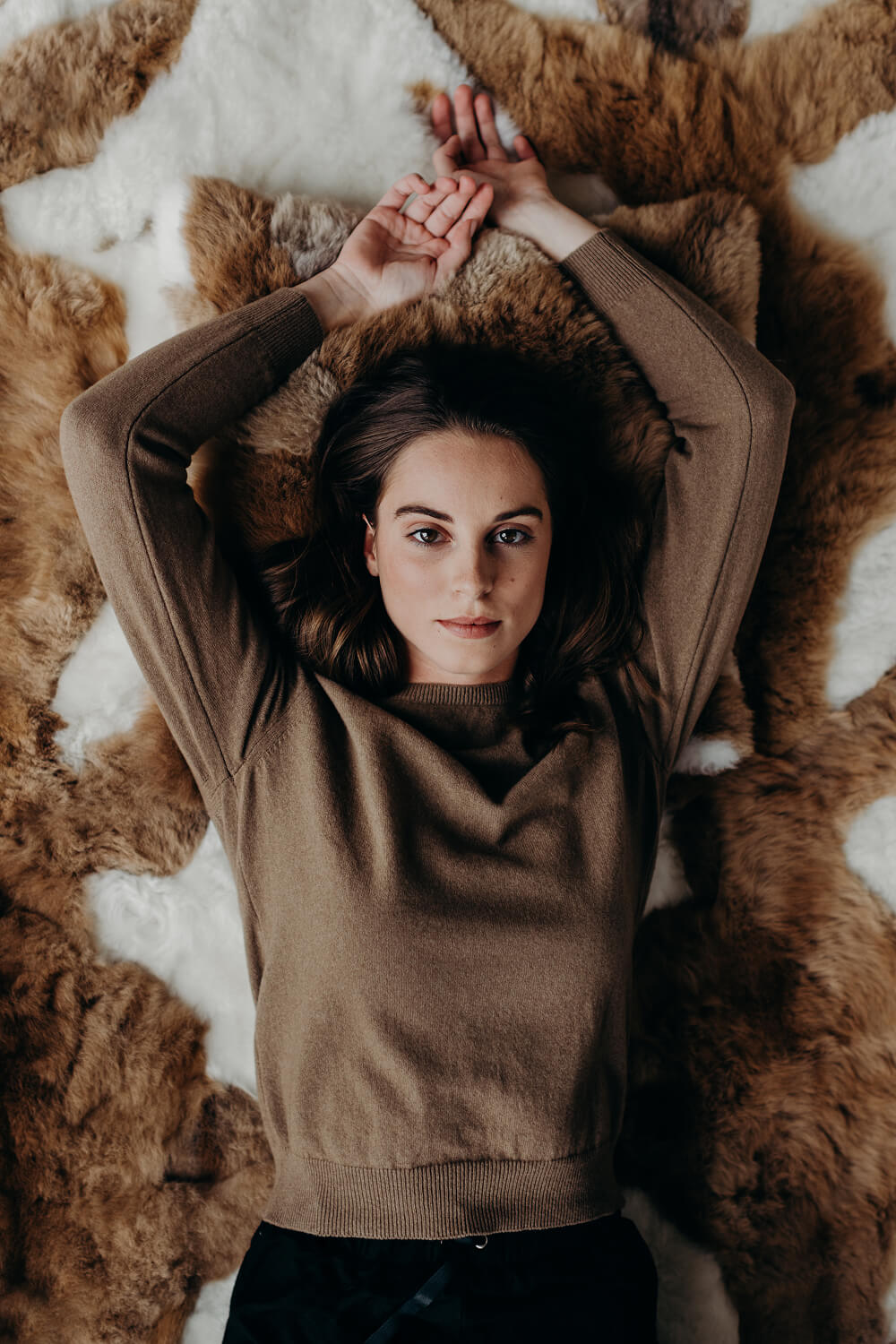 Woman lying on a textured brown rug wearing a brown sweater.