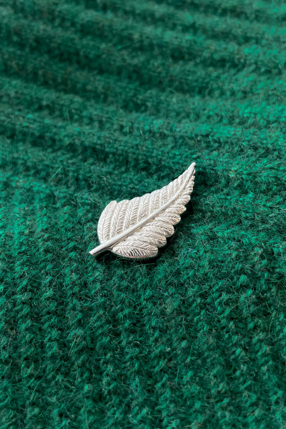 Silver leaf-shaped brooch on a green textured fabric background