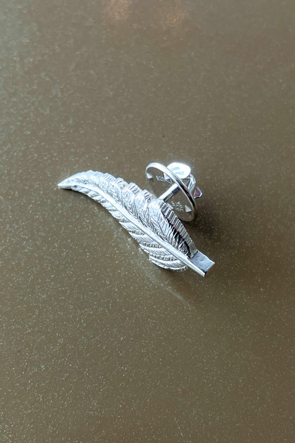 Silver feather-shaped earring on a brown surface