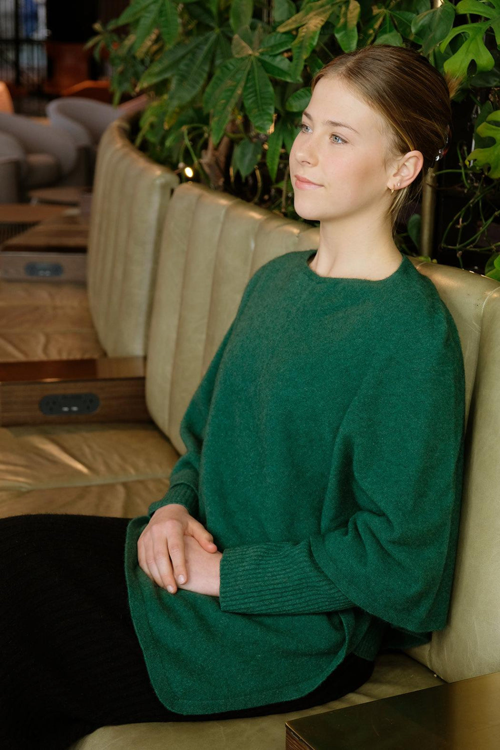 Woman wearing a green leaf poncho sitting on sofa