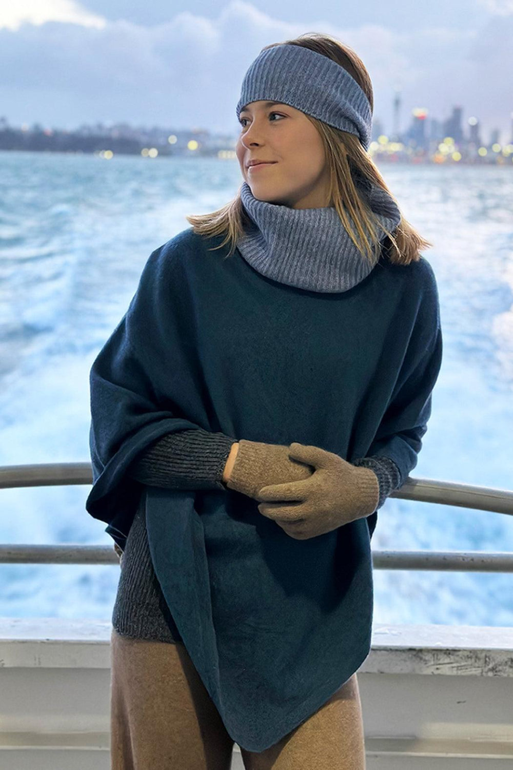 Woman wearing a blue poncho with light blue neckwarmer and head band on ship.