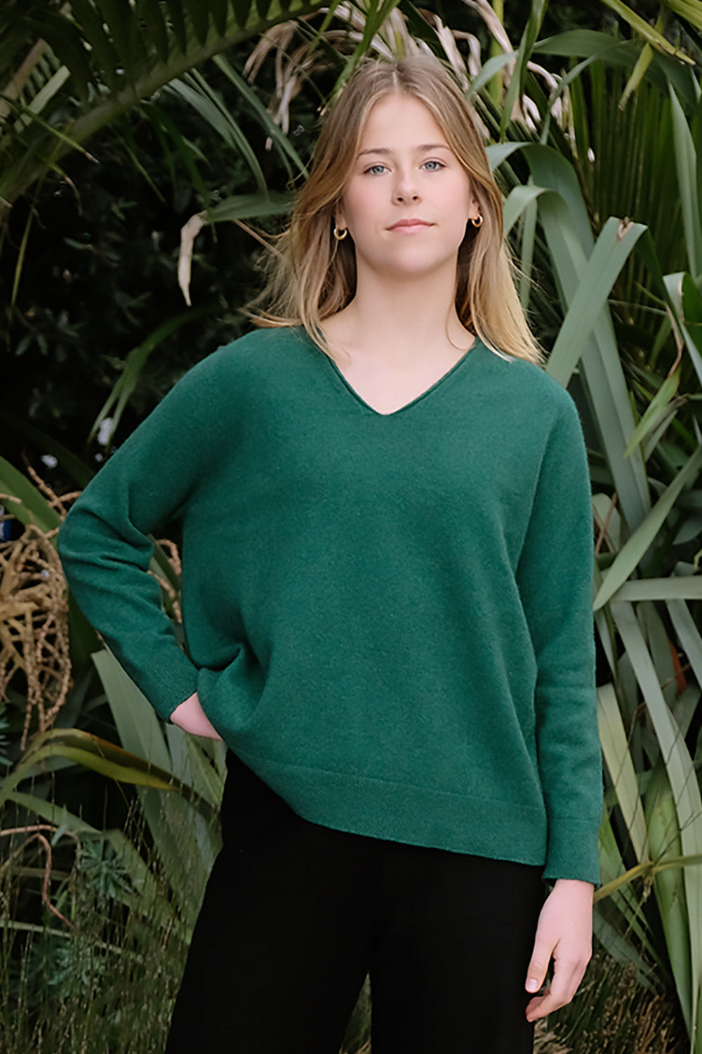 Woman wearing a green sweater standing in front of green plants