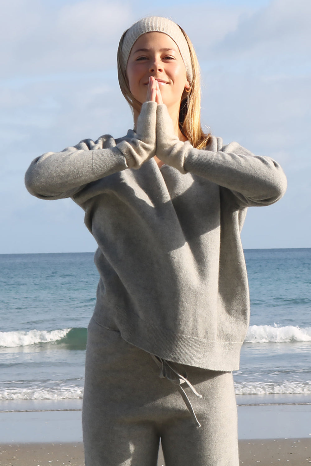Person in beige outfit standing on a beach with ocean waves in the background