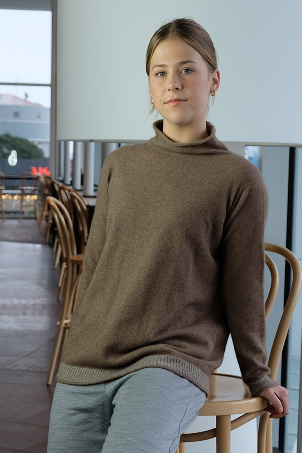 Person wearing a brown sweater sitting on a chair indoors