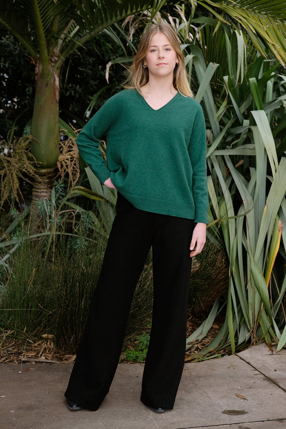 A woman standing outside wearing black merino active pants and a green sweater.