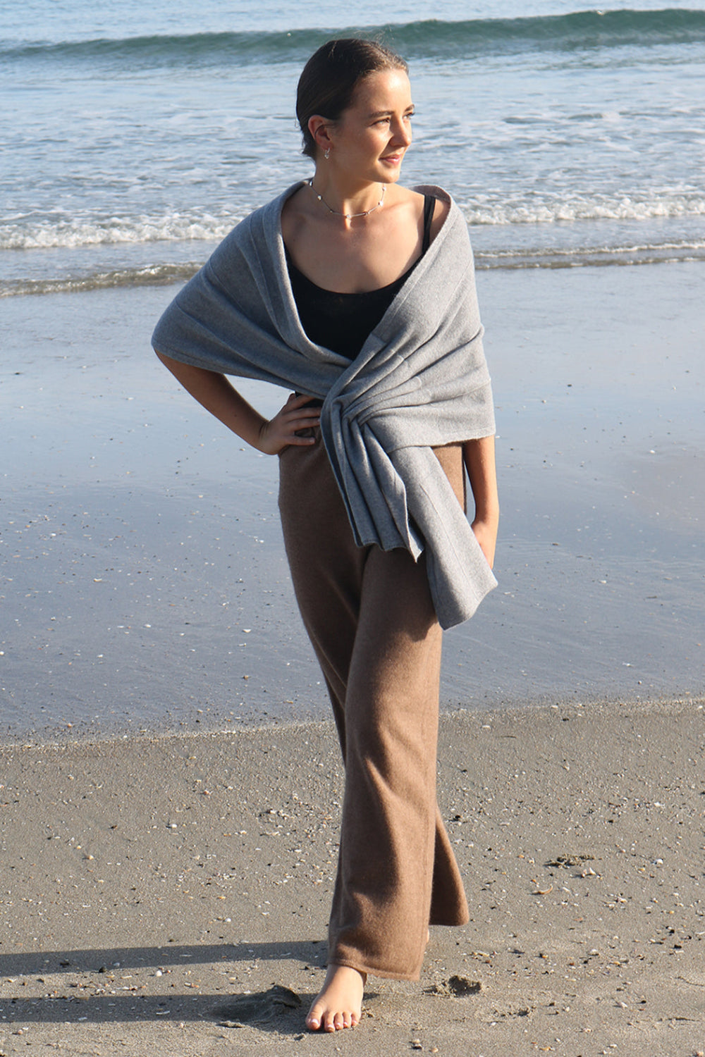 A woman standing on a beach wearing black merino active pants and a light-colored sweater.
