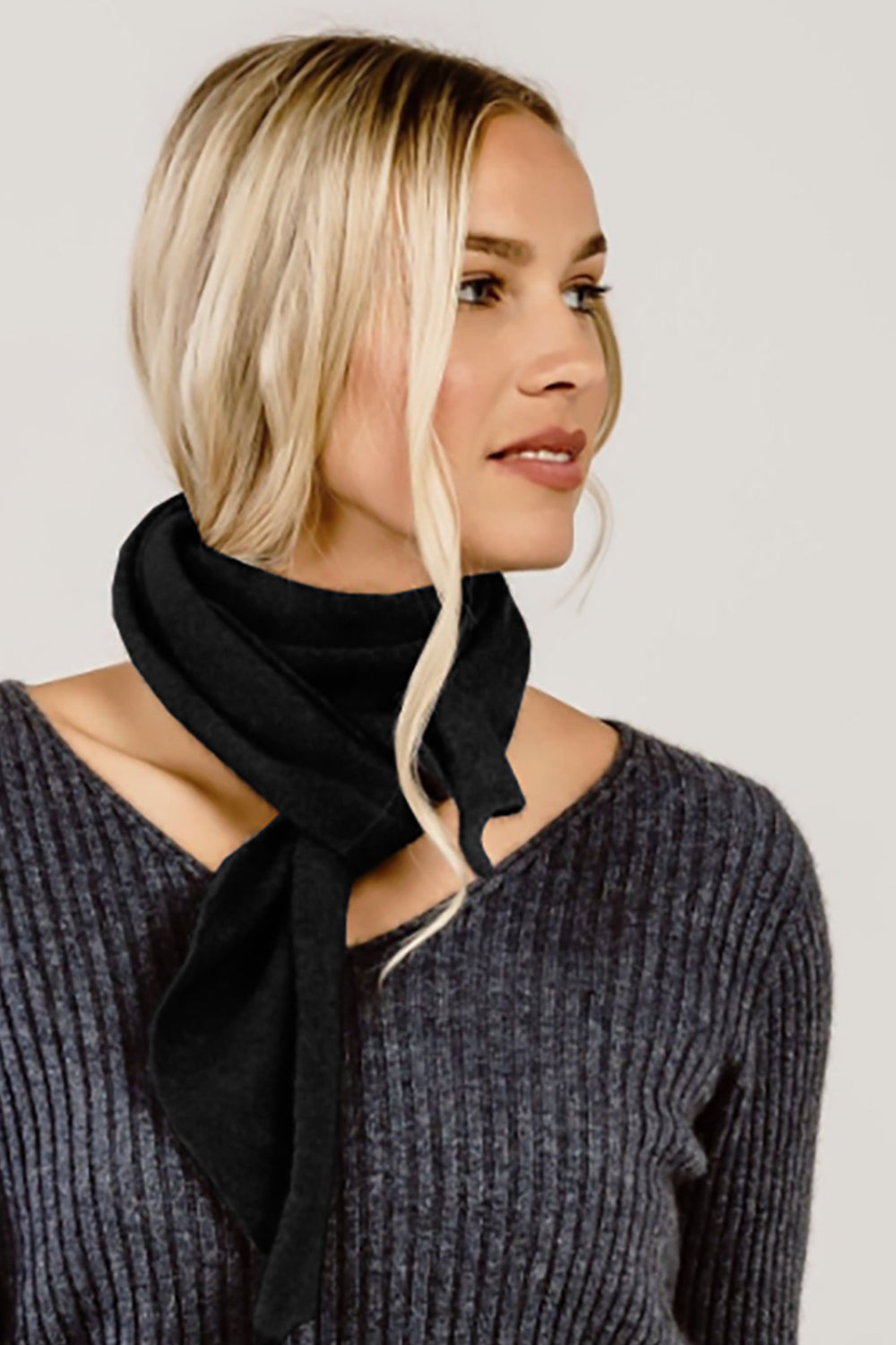 Woman wearing a black scarf and gray sweater against a plain background