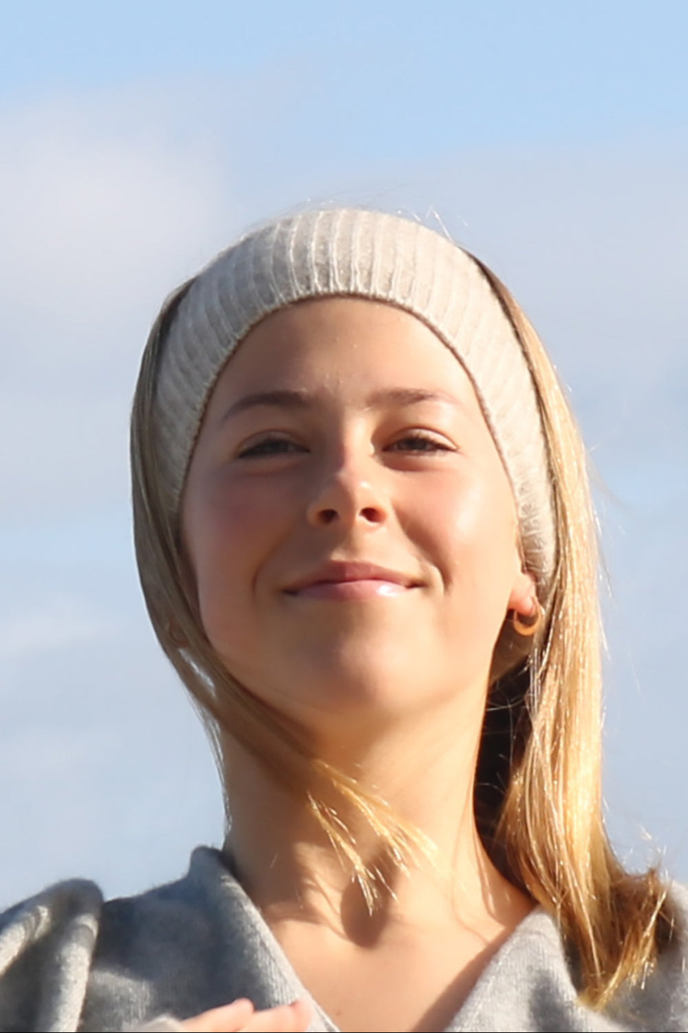 A woman wearing a beige merino possum blend headband, smiling outdoors.
