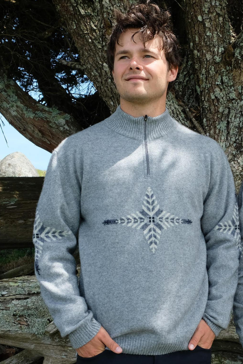 Man wearing a gray sweater with a snowflake design outdoors.