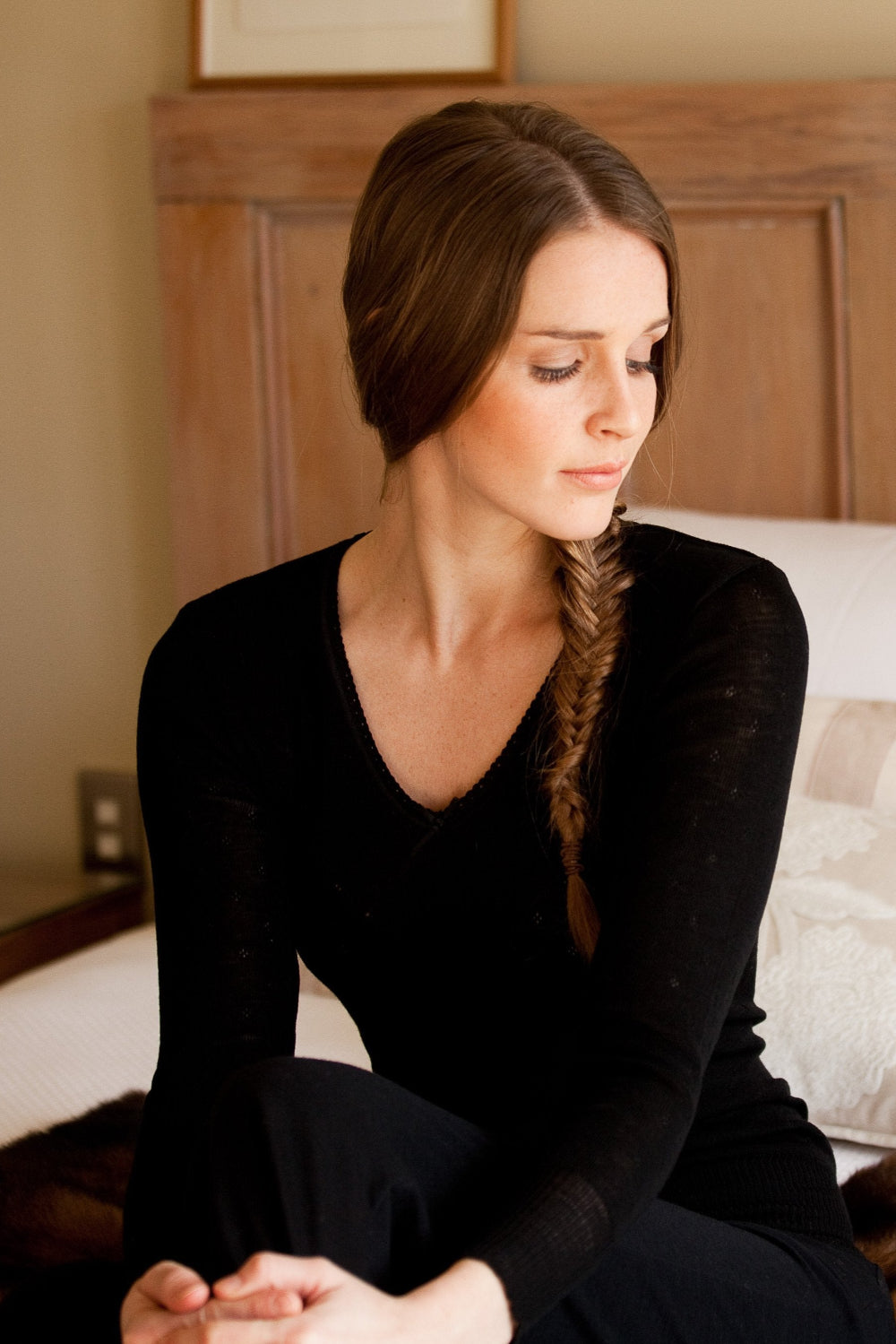 A woman sitting and wearing a long sleeve black merino thermal top with a V-neck.