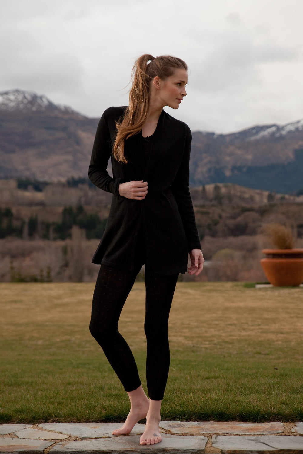 Woman in black outfit standing in a scenic outdoor setting with mountains in the background
