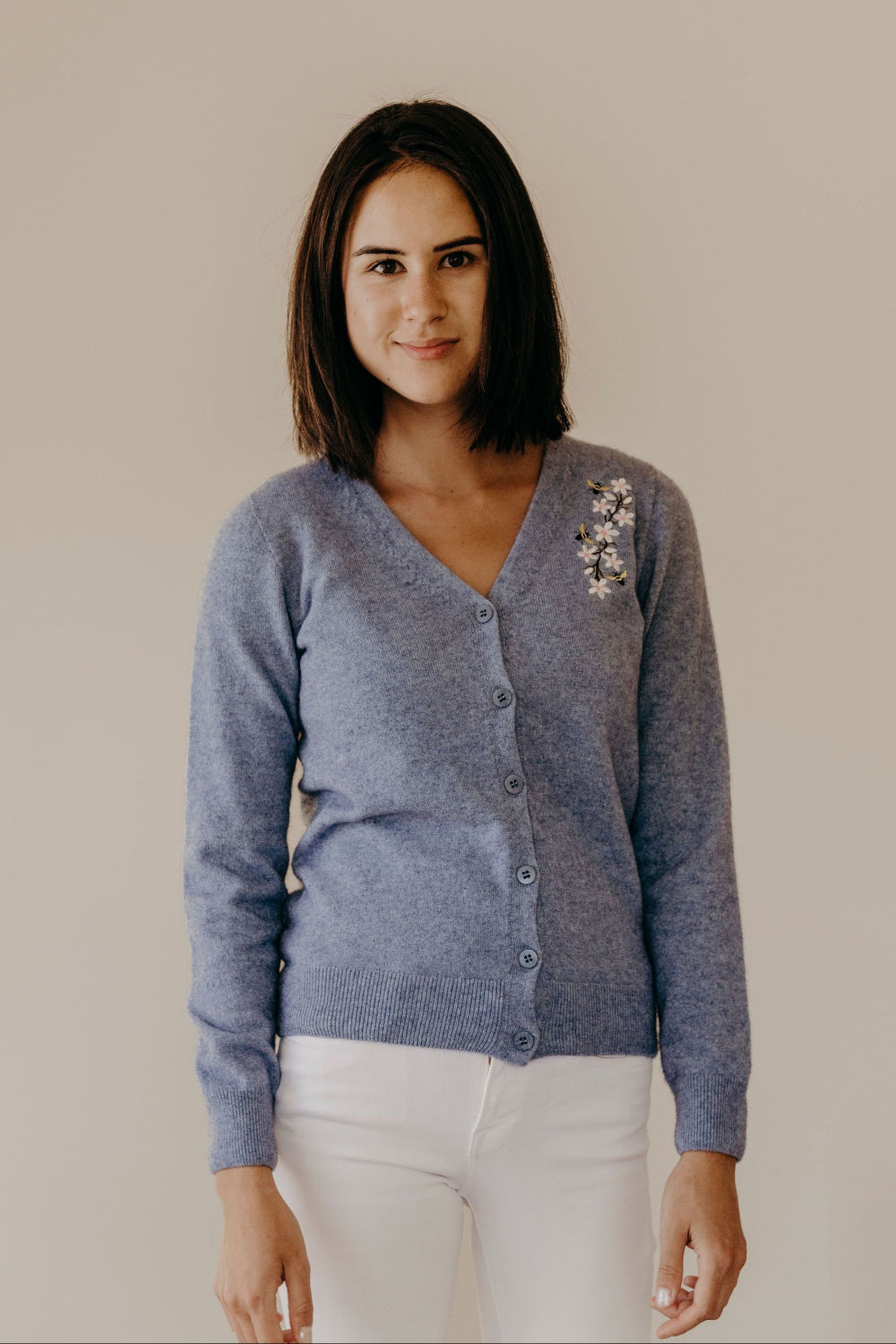 A woman wearing a blue Merinosilk Manuka Cardigan with button-closure, featuring embroidery of Manuka flowers and bees.