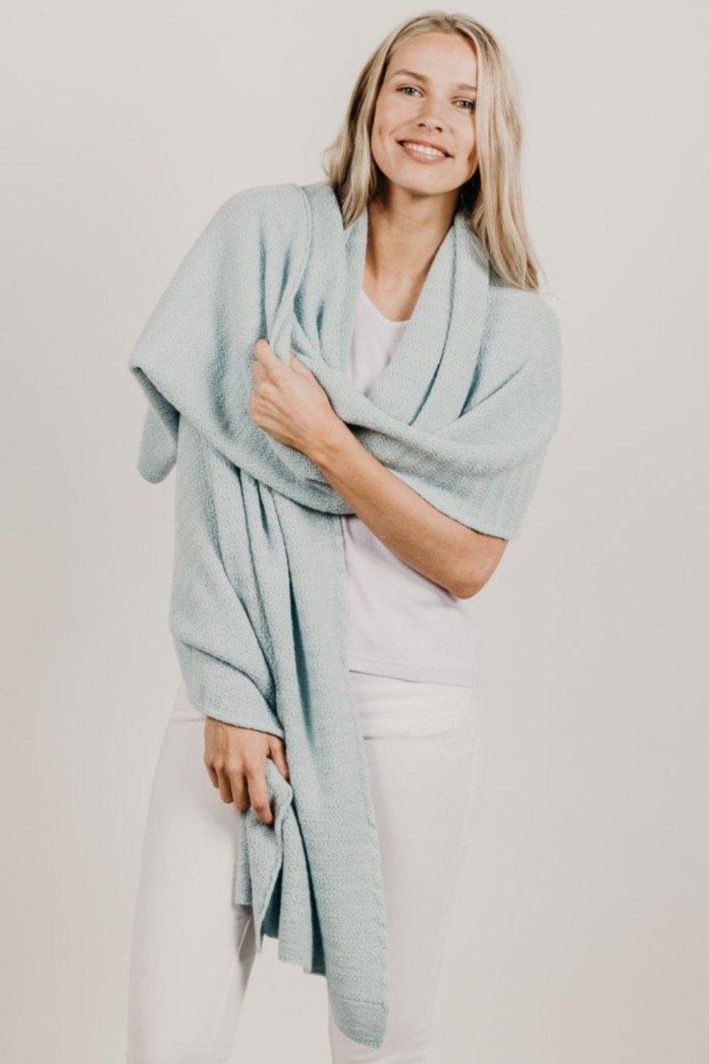 A woman smiling and wrapping a light blue alpaca wool shawl around her shoulders.