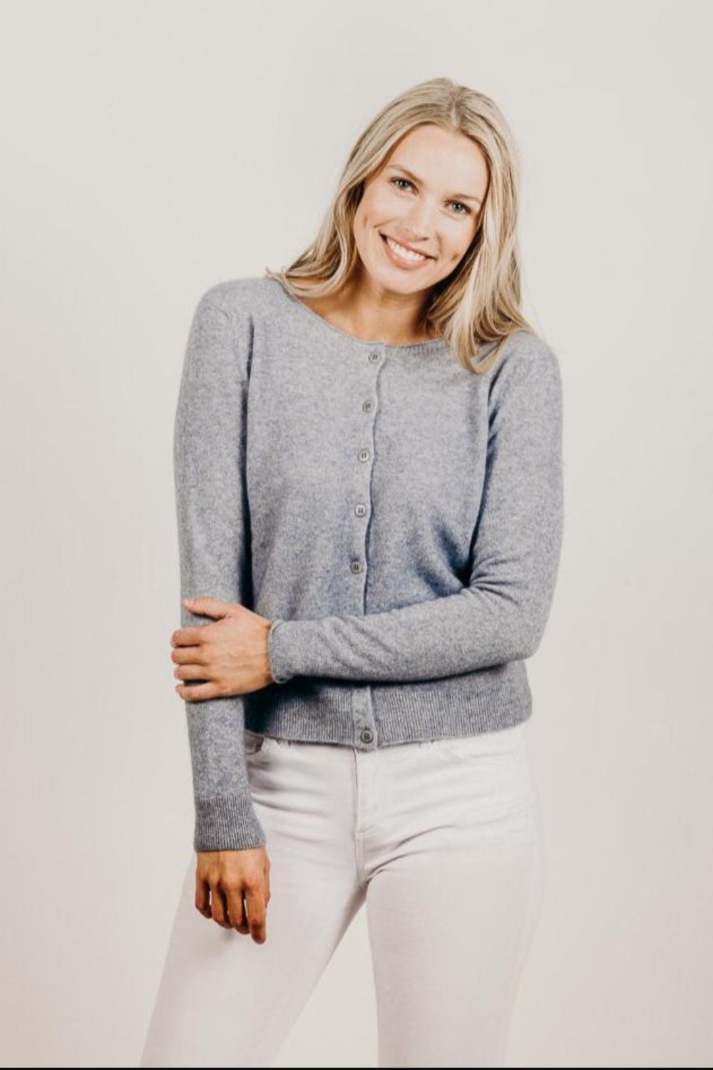 Woman wearing a gray cardigan and white pants against a plain background