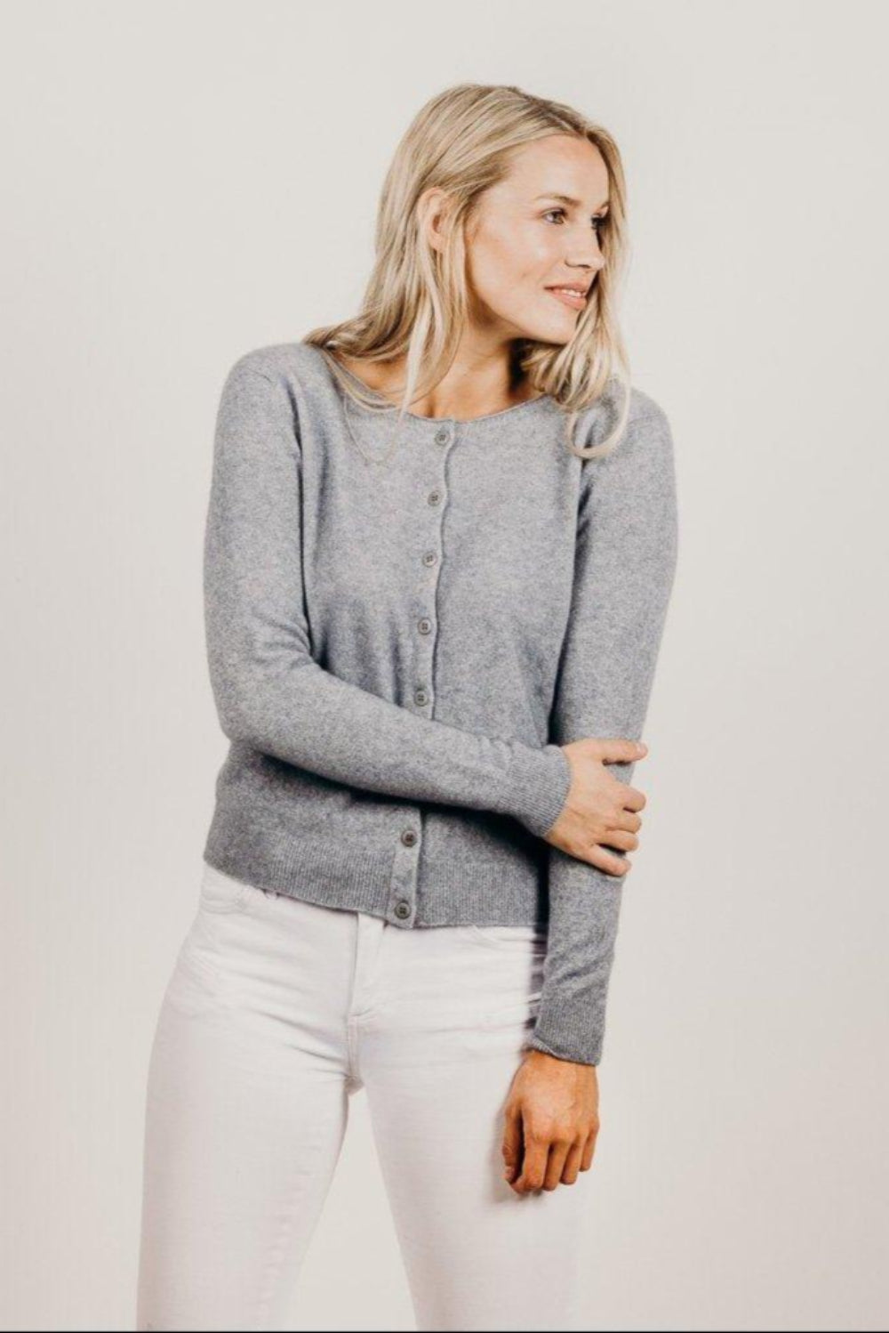 Woman wearing a gray cardigan and white pants against a plain background