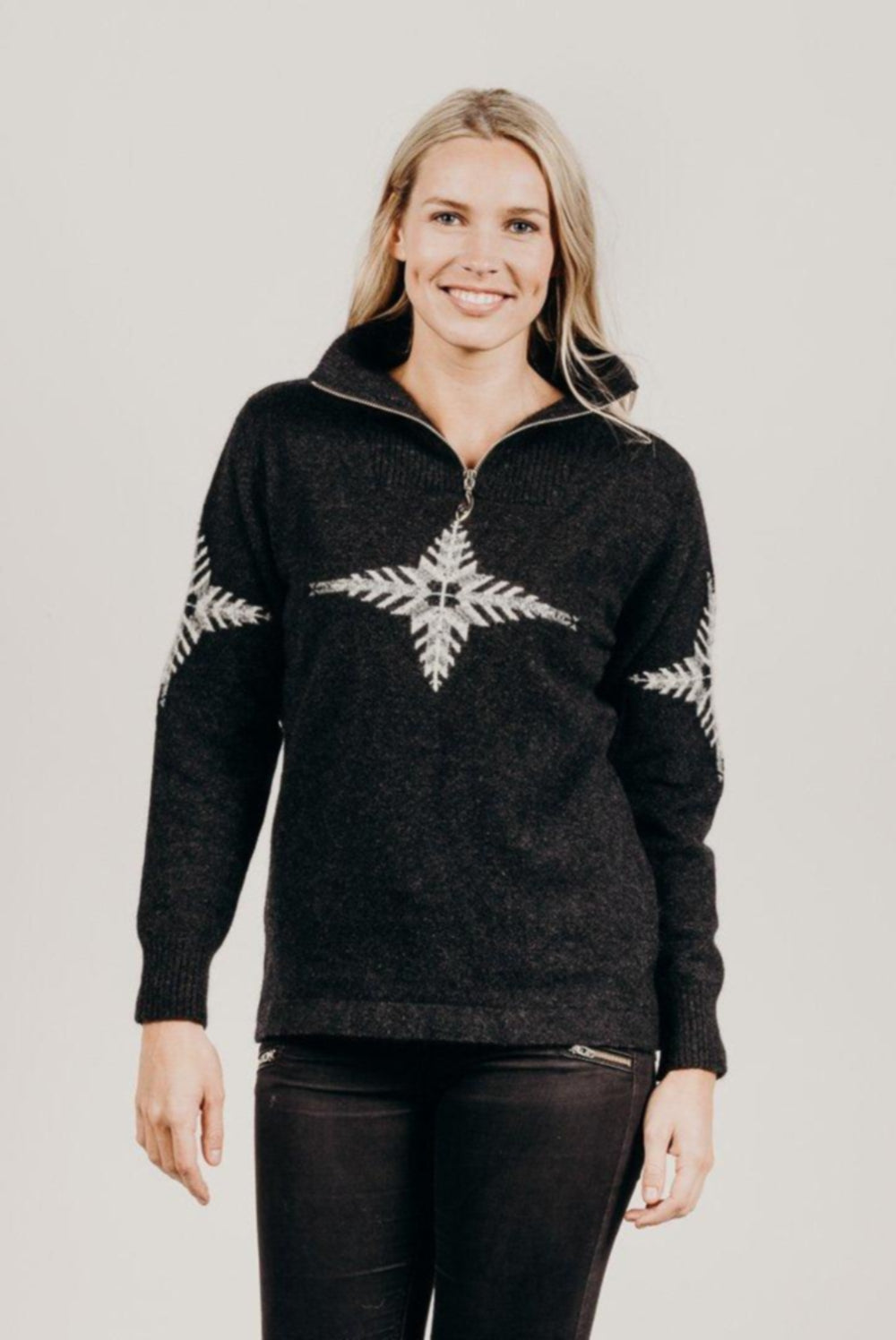 Woman wearing a black zip sweater with a white snowflake design on a plain background