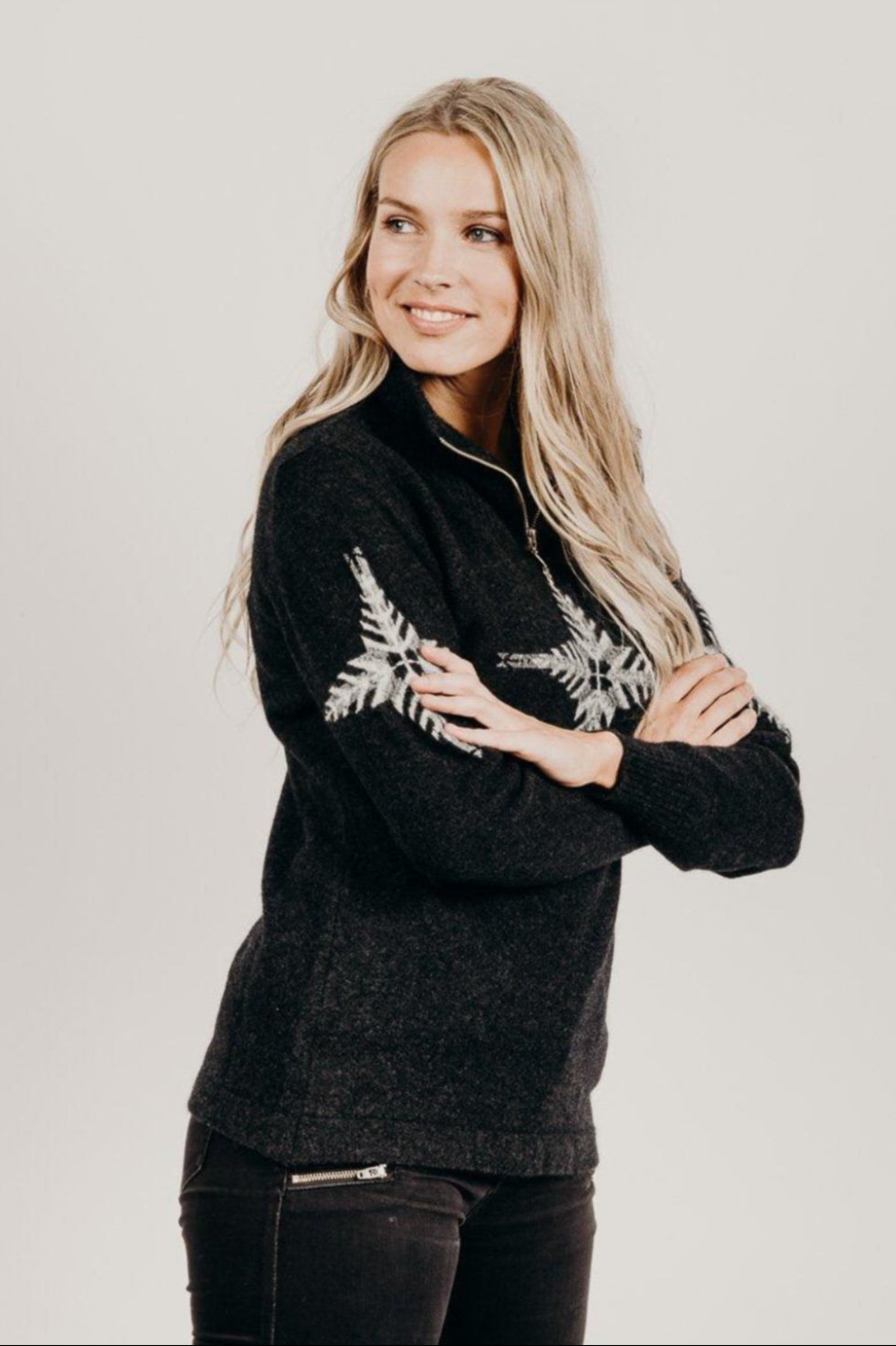 Woman wearing a black zip sweater with white snow flake patterns on a plain background