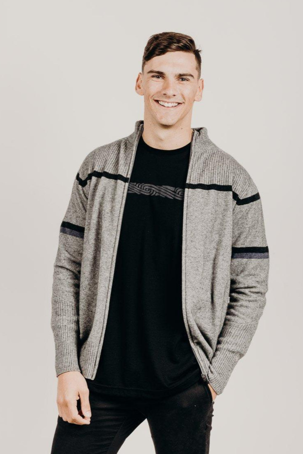 Man wearing a gray zip jacket with black stripes on a plain background