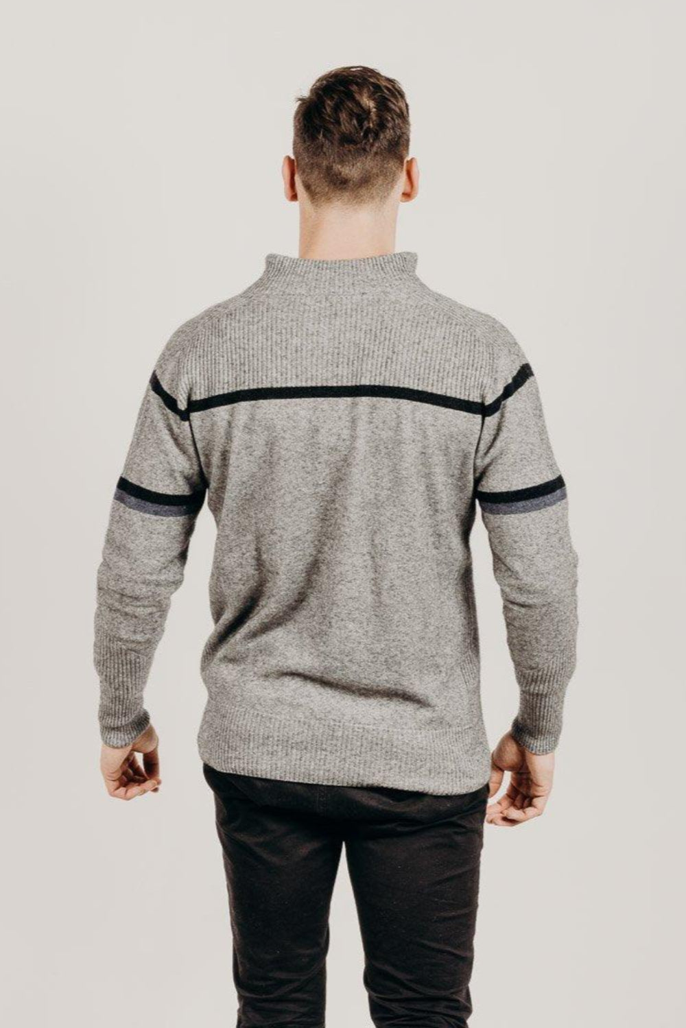 Man wearing a gray sweater with black accents on a plain background