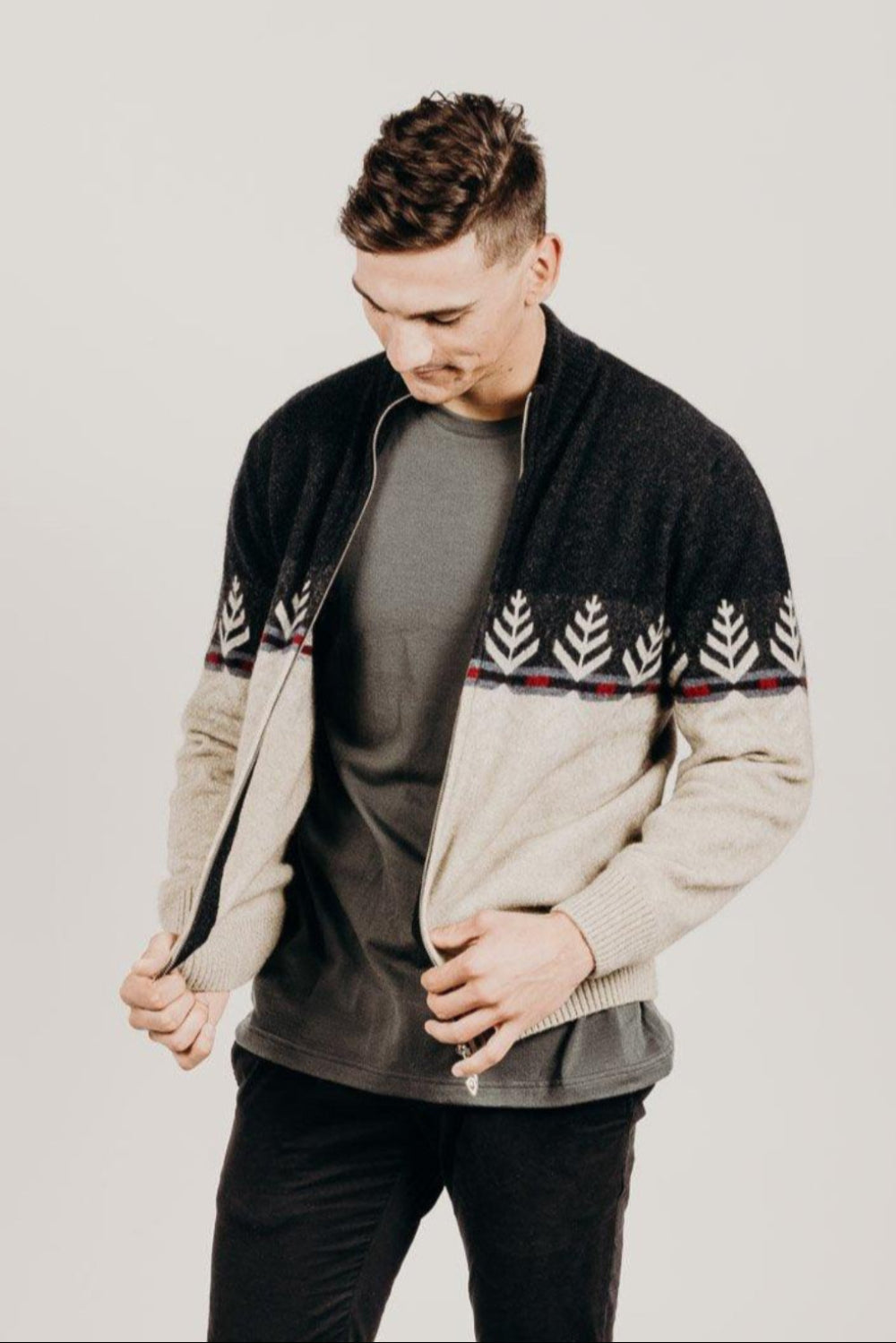Man wearing a black and beige patterned sweater over a gray shirt on a plain background