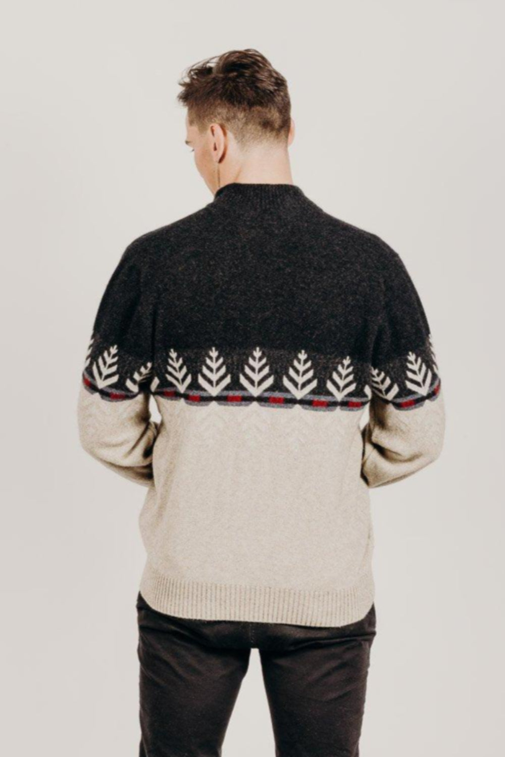 Man wearing a black and beige patterned sweater on a plain background