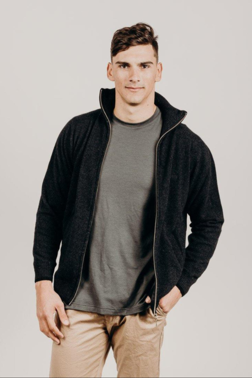 A man wearing a black Merinosilk pocket jacket with a full zip and standing with hands in pockets.