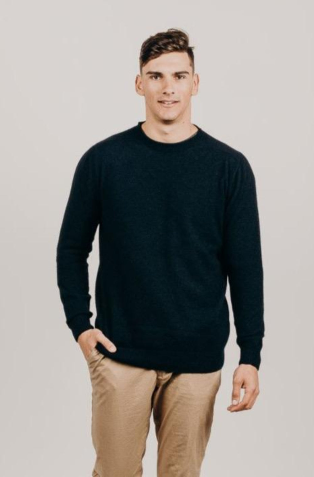Man wearing a navy sweater and beige pants against a plain backgroundnavy