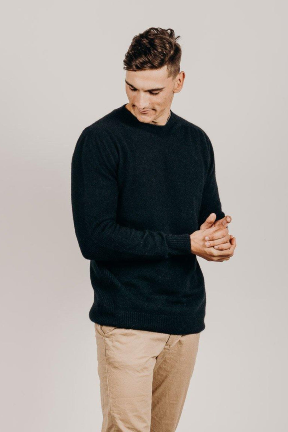Man wearing a navy sweater and beige pants against a plain background