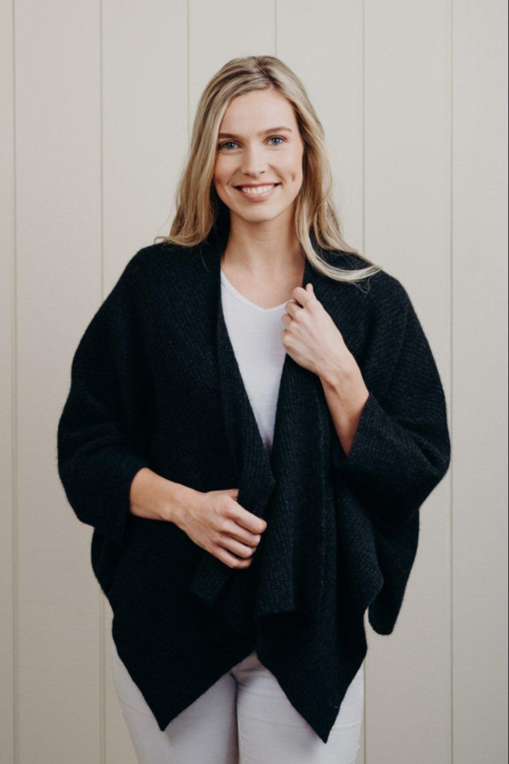 Woman wearing a black cardigan over a white top against a light background
