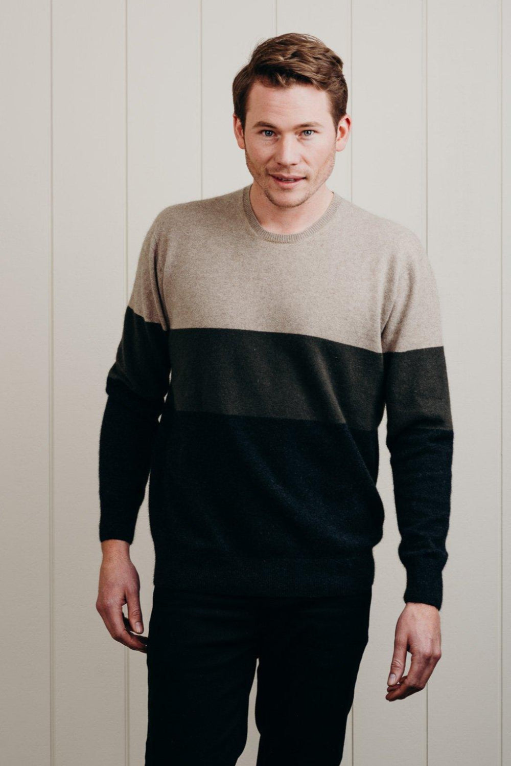 Man wearing a two-tone sweater against a light wooden panel background