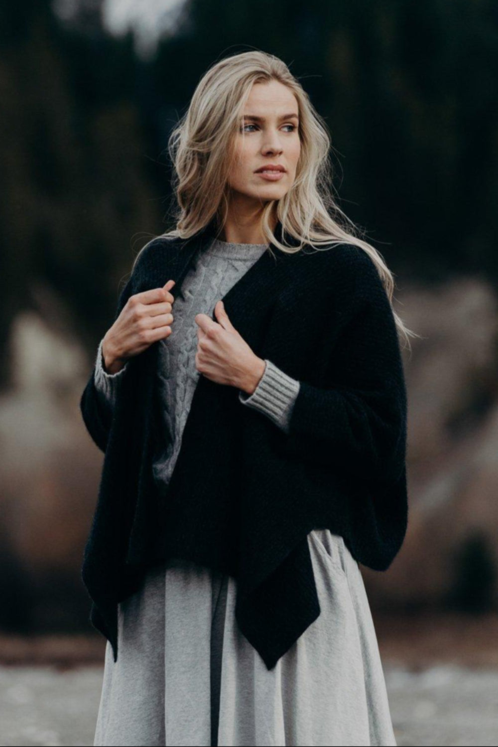 Woman wearing a black wrap over a gray sweater with a blurred natural background