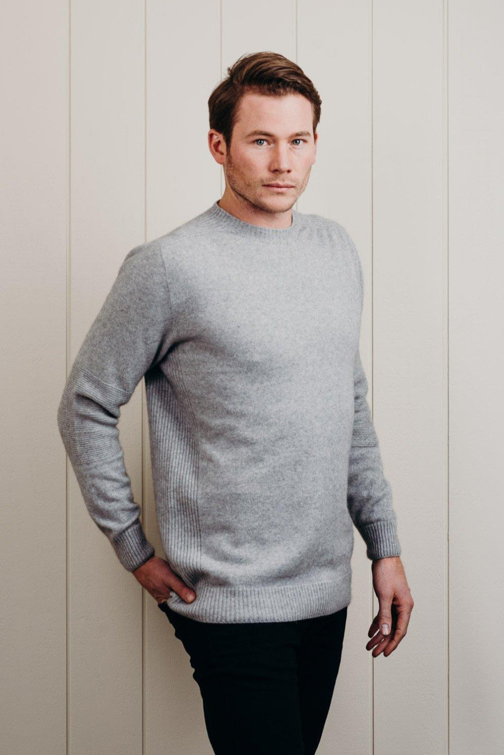 Man wearing a gray sweater against a light wooden panel background