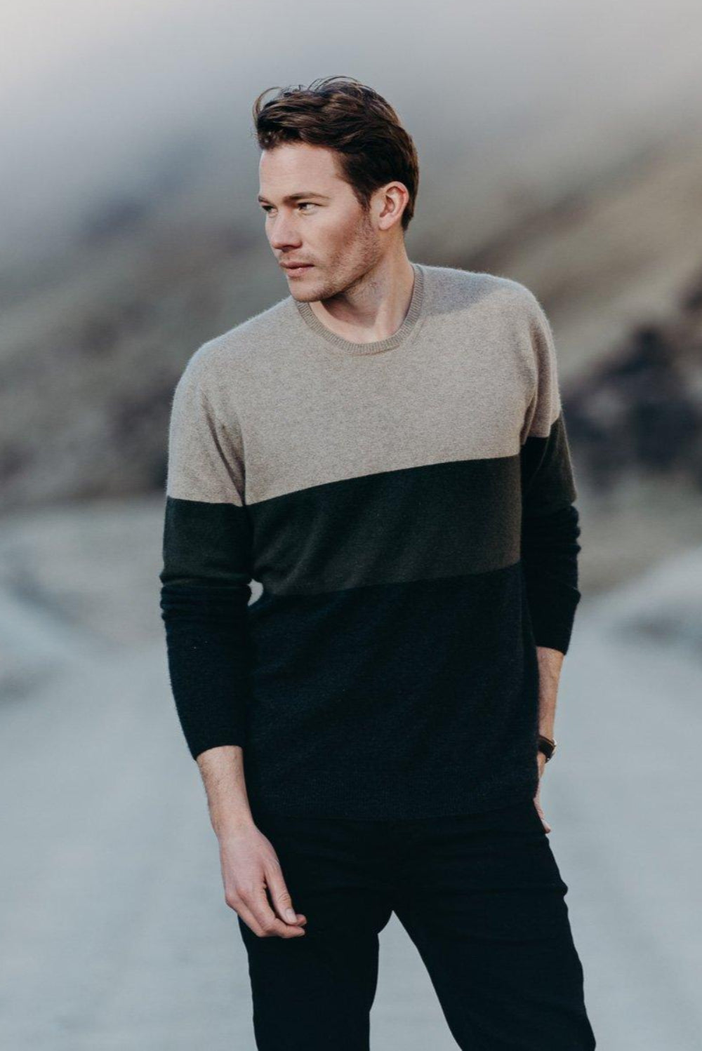 Man wearing a two-tone sweater standing in a mountainous landscape