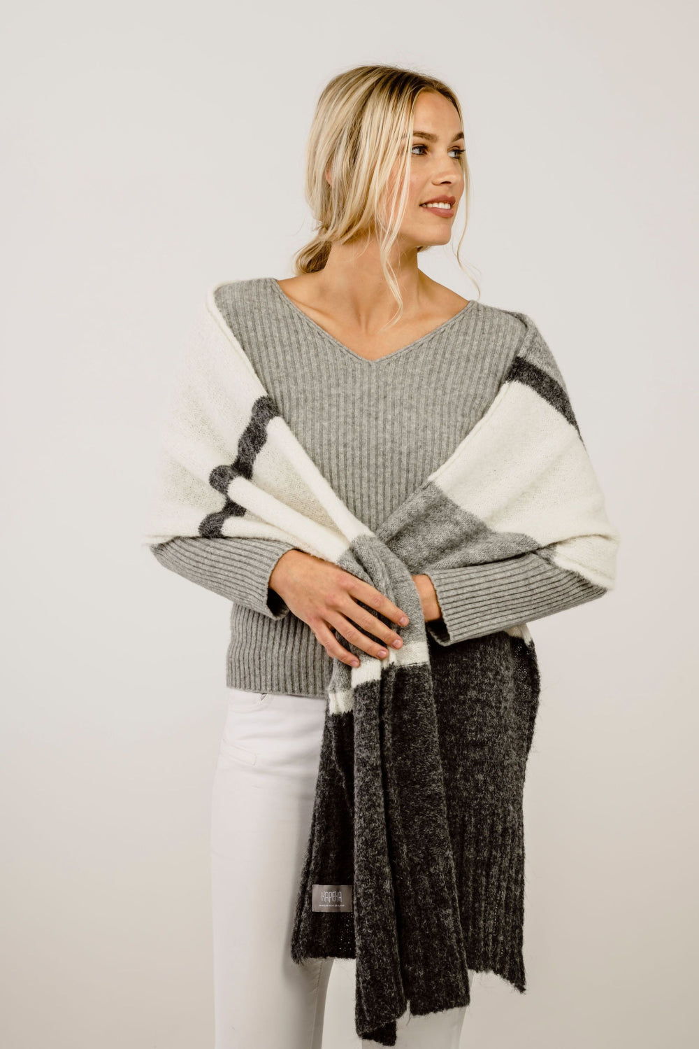 Woman wearing a gray sweater with a scarf against a plain background