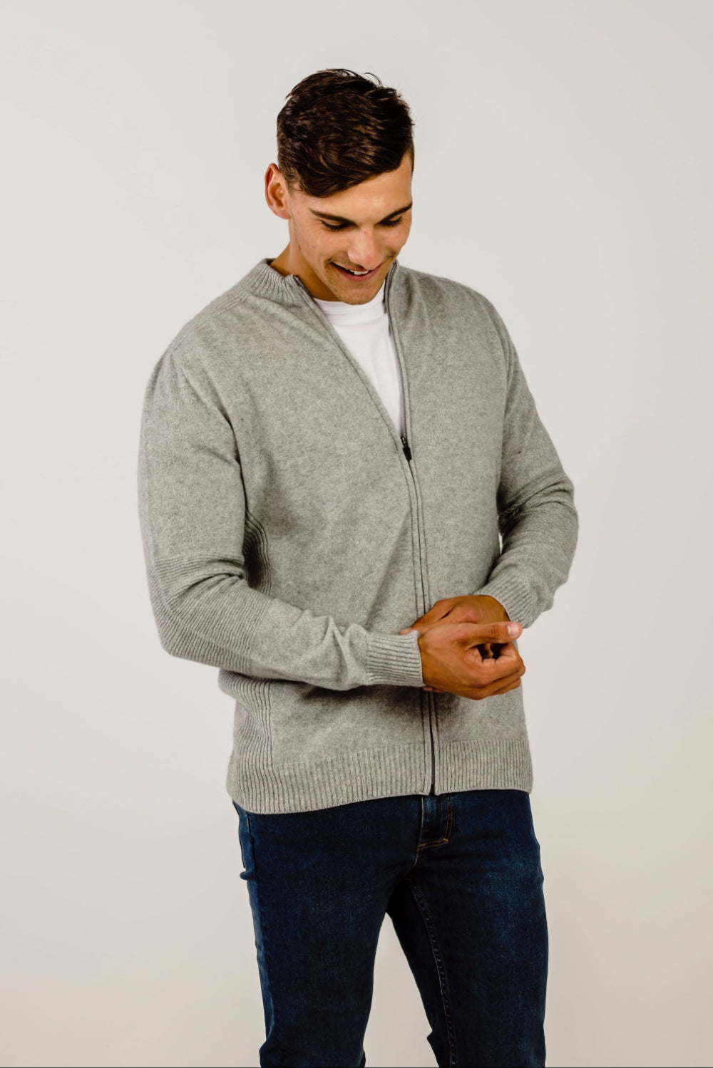 Man wearing a gray zip-up sweater over a white shirt, standing against a plain background