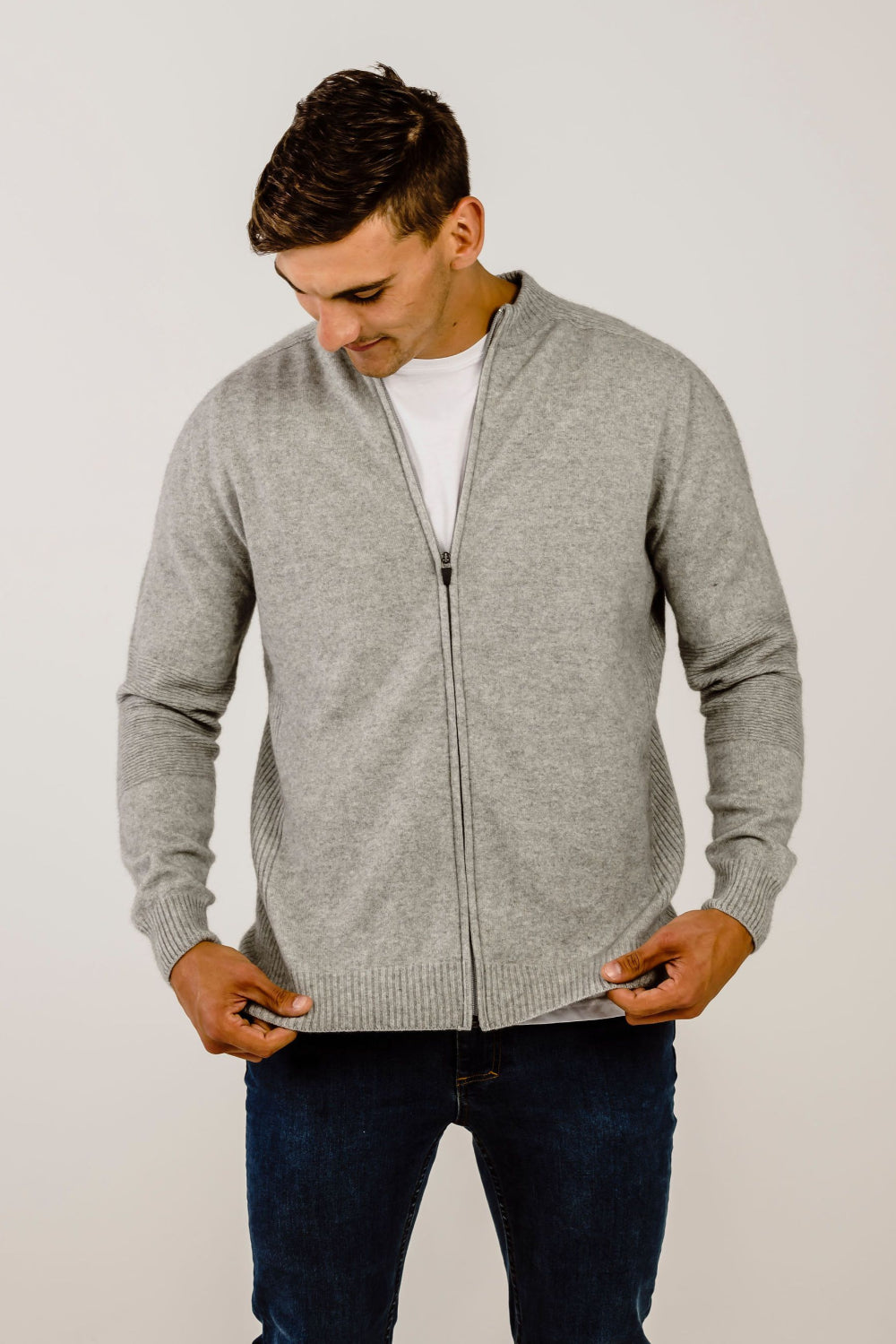 Man wearing a gray zip-up sweater over a white shirt on a plain background