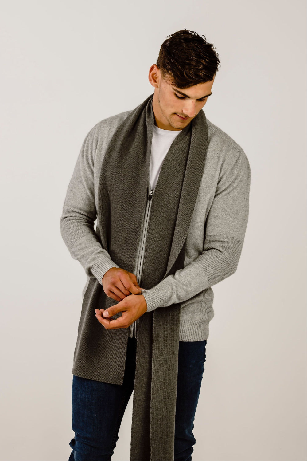 Man wearing a long gray cardigan with a matching scarf on a plpain background