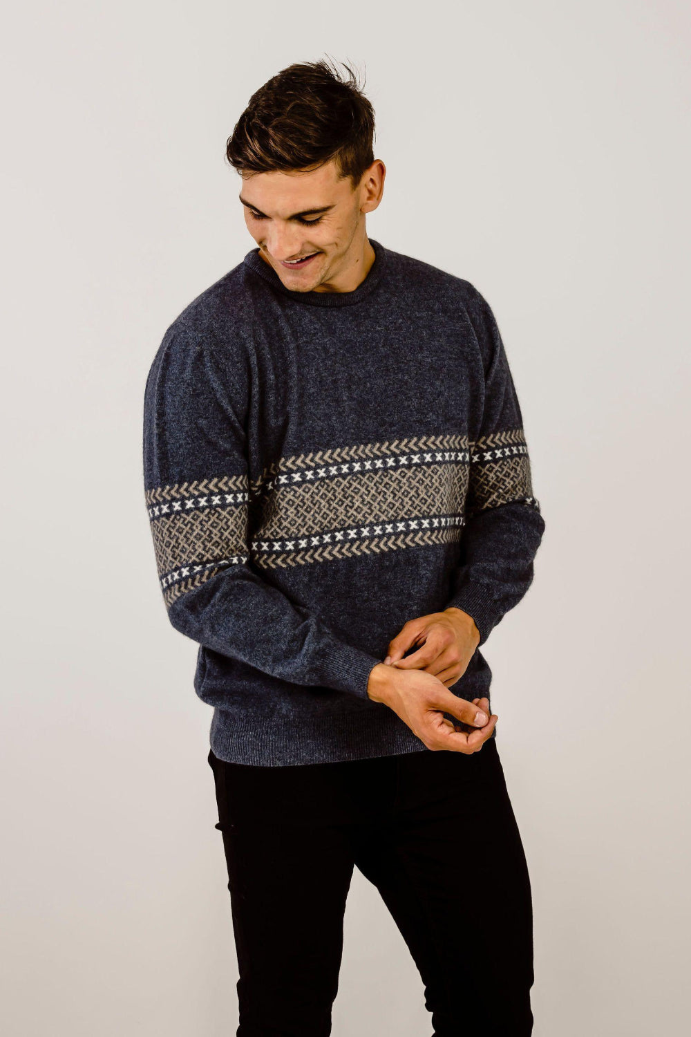 Man wearing a dark blue sweater with a patterned design on a plain background
